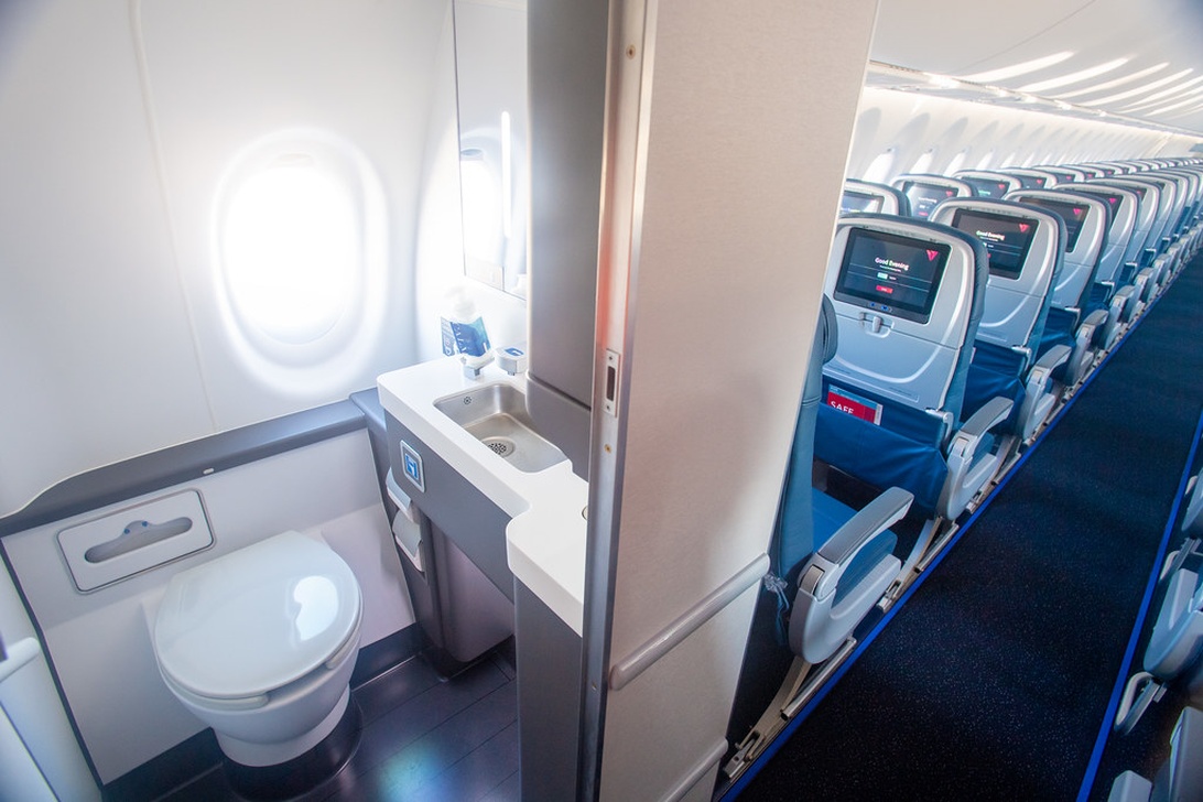Interiør af en flykabine med passagersæder og et flytoilet, der illustrerer omgivelserne ombord.